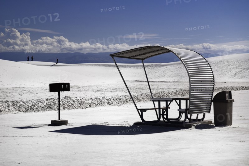 USA, New Mexico, Otero County, White Sands National Monunment. Landscape of white sand with dramatic cloudscape above. Seating area and distant figures. 
Photo : Hugh Rooney