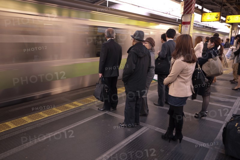 Japan, Honshu, Tokyo, Commuters waiting on platform whilst train speeds through without stopping. 
Photo : Jon Burbank