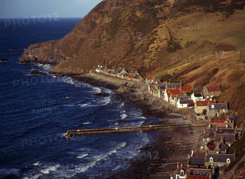 Scotland, Aberdeenshire, Crovie, One time fishing village seen from cliff top. Row of cottages at foot of steep hillside overlooking coast and stone jetty. 
Photo : Bryan Pickering