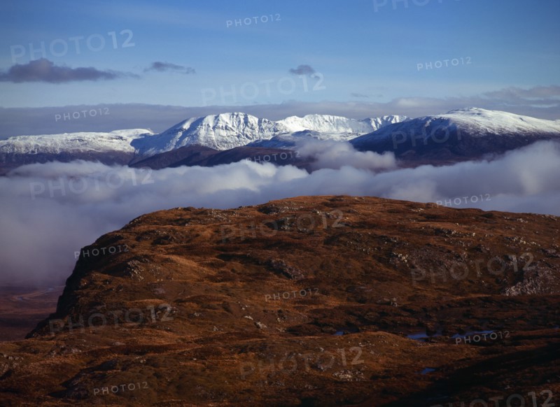 Scotland, Highlands, West, Ben More Forest and snow covered Assynt Mountains 998 metres at highest point above thick white cloud on skyline. View from Knockan Crag. 
Photo : Bryan Pickering