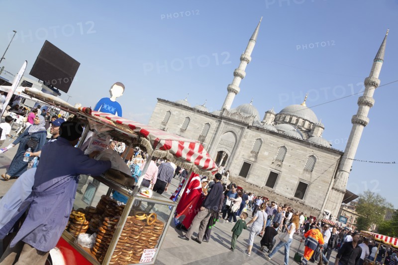 Turkey, Istanbul, Eminonu Yeni Camii New Mosque with pretzel vendor in the square. 
Photo : Stephen Rafferty