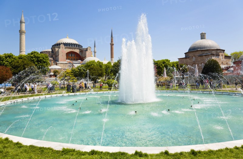 Turkey, Istanbul, Sultanahmet Haghia Sophia with dome and minarets beyond the water fountain and Baths of Roxelana in the gardens with sightseeing tourists. 
Photo : Paul Seheult