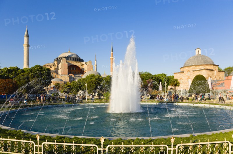 Turkey, Istanbul, Sultanahmet Haghia Sophia with dome and minarets beyond the water fountain and Baths of Roxelana in the gardens with sightseeing tourists. 
Photo : Paul Seheult