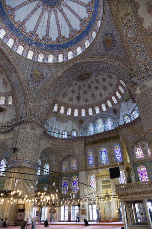 Turkey, Istanbul, Sultanahmet Camii The Blue Mosque interior with people at prayer beneath chandeliers and decorated domes above and stained glass windows beyond. 
Photo : Paul Seheult