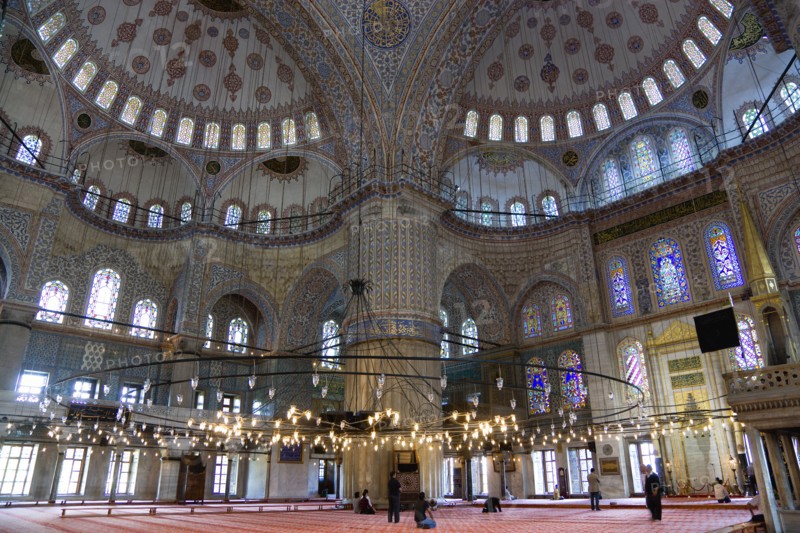 Turkey, Istanbul, Sultanahmet Camii The Blue Mosque interior with people at prayer beneath chandeliers and decorated domes above and stained glass windows beyond. 
Photo : Paul Seheult