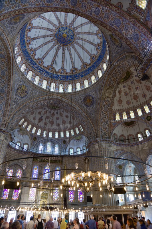 Turkey, Istanbul, Sultanahmet Camii The Blue Mosque interior with sightseeing tourists by a chandelier below the decorated domes with stained glass windows beyond. 
Photo : Paul Seheult