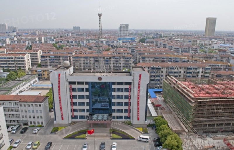 China, Jiangsu, Qidong, Bureau of Public Security with Chinese flag flying in forecourt and radio communications mast on the roof; red banners with Chinese characters hanging from building City skyline and new construction. 
Photo : Trevor Page