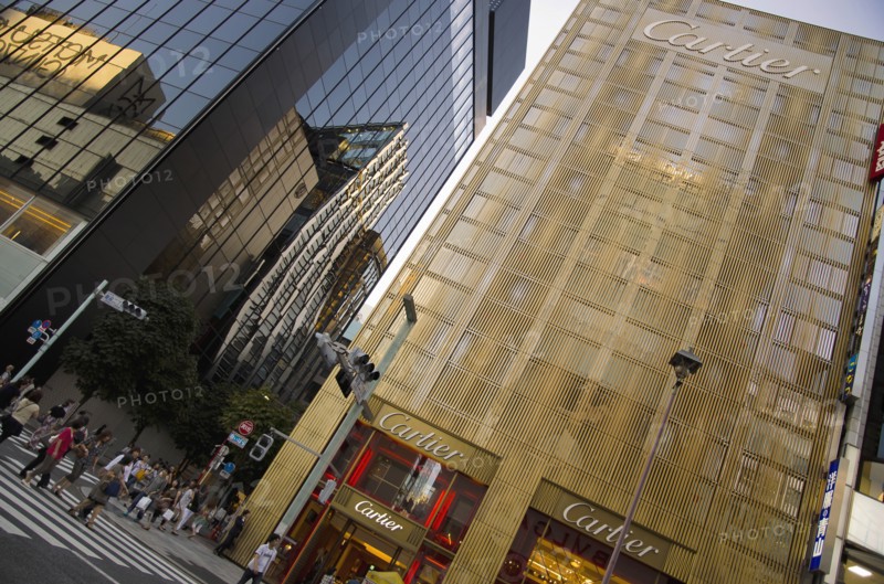 Japan, Honshu, Tokyo, Ginza Golden facade of the Cartier Building with the Chanel Building on left and DeBeers curved facade reflected in black glass on Chuo-dori Avenue. 
Photo : Jon Burbank