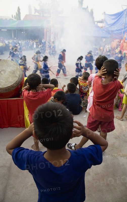 Thai boys cover their ears watching performance with firecrackers exploding at local temple.