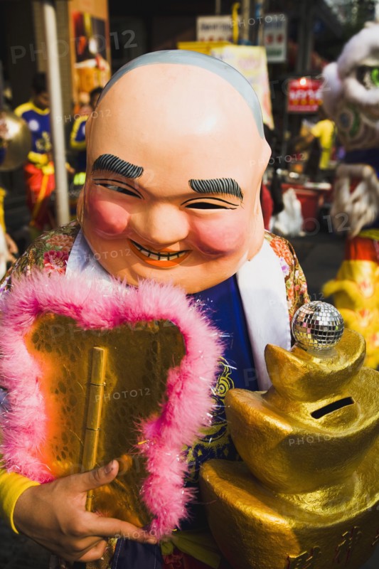 Member of dance troupe with papier mache character head and fan collecting money for Chinese New Year show.