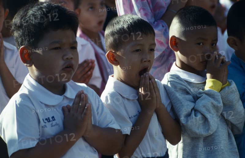 Buddhist Schoolchildren with hands held in prayer one child yawning.