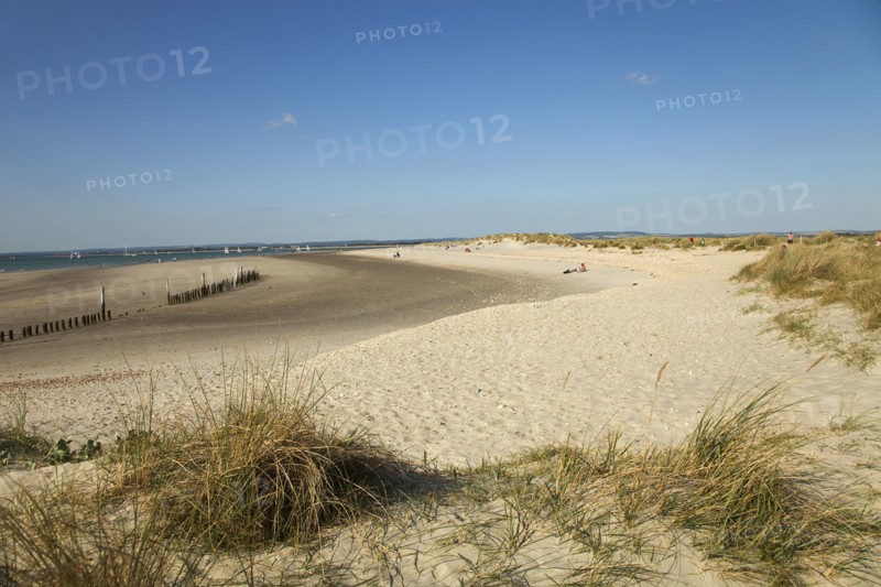 View across sand dunes towards beach and sea at East Head. Sunshine and blue sky.