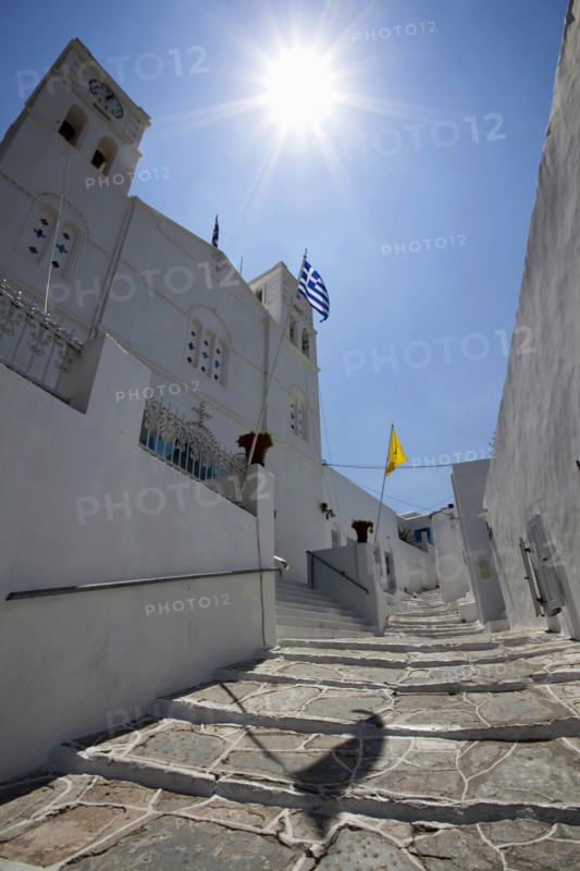 Portrait format low angle photograph of a typical alley found only at Cyclades island complex with the church of Agios Spyridonas on the left hand side.