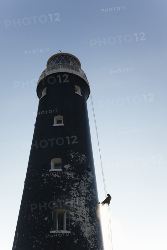 Man cleaning Lighthouse tower with pressure washer whilst abseiling.