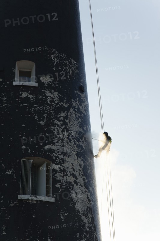 Man cleaning Lighthouse tower with pressure washer whilst abseiling.
