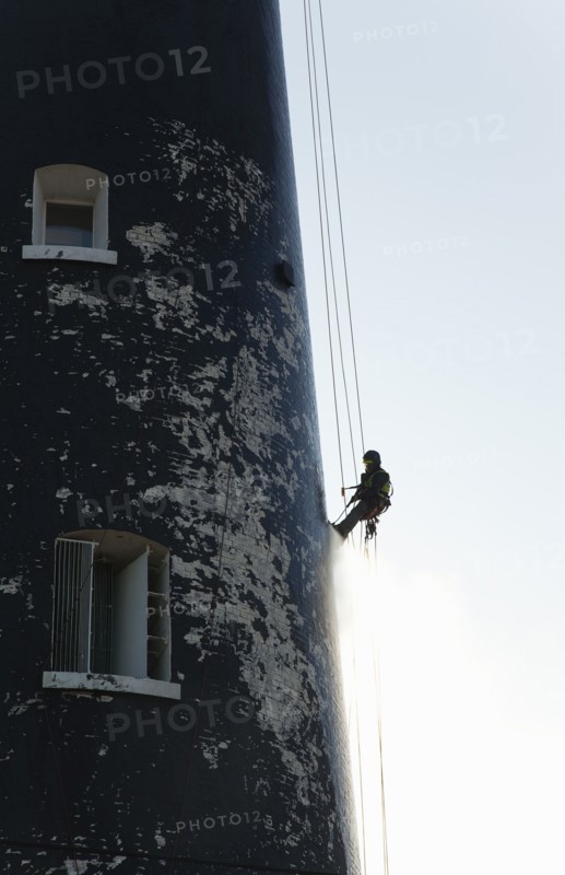 Man cleaning Lighthouse tower with pressure washer whilst abseiling.
