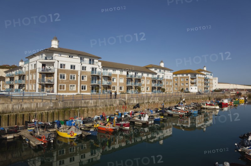 View over fishing boats moored in the Marina with apartment buildings behind.