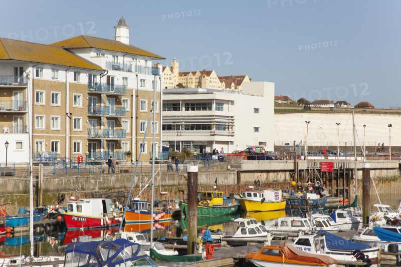 View over fishing boats moored in the Marina with apartment buildings behind.