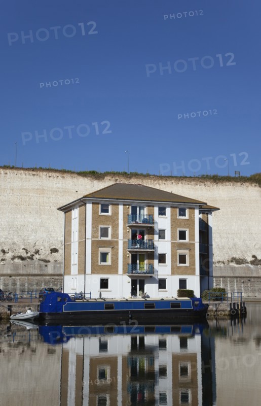 Apartment building in marina with moored barge and chalk cliffs behind.