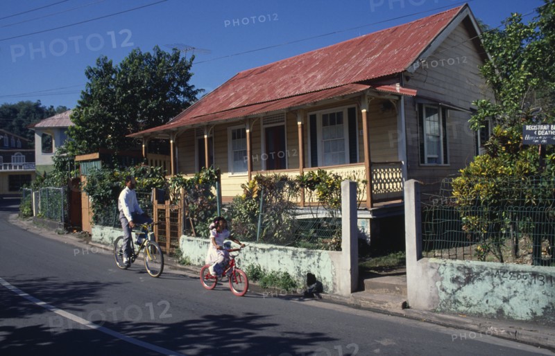 West Indies, Jamaica , Port Antonio, Roadside housing with veranda and walled garden. Boy and young girl cycling past. Photo : David Cumming