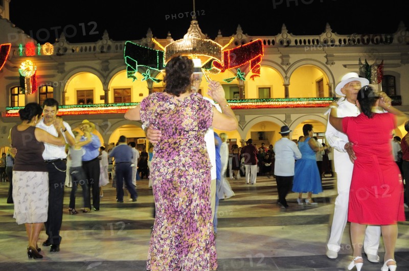 Mexico, Veracruz, Couples dancing in the Zocalo at night illuminated decorations in the national colours for Independence Day celebrations on building facade behind. Photo : Nick Bonetti