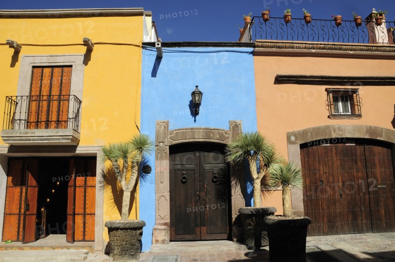 Mexico, Bajio, San Miguel de Allende, Colourful house facades on paved street with plant pots on roof balcony and outside wooden doors. Photo : Nick Bonetti