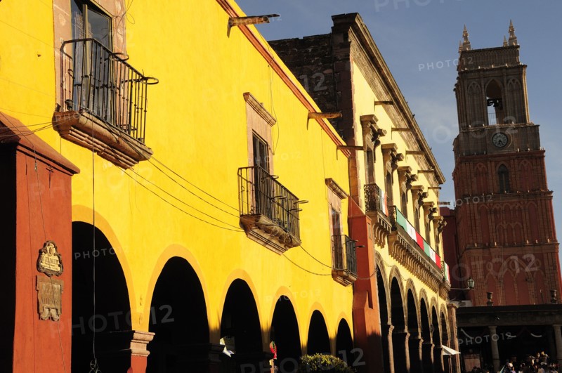 Mexico, Bajio, San Miguel de Allende, El Jardin Yellow facade of colonial mansion and arcades with clock tower beyond. Photo : Nick Bonetti