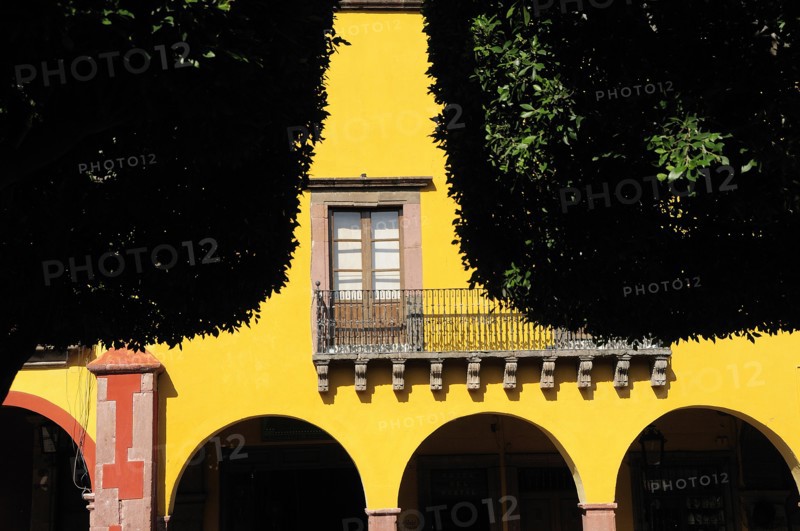 Mexico, Bajio, San Miguel de Allende, El Jardin Detail of yellow painted facade of colonial mansion with French window and balcony part framed by trees in foreground. Photo : Nick Bonetti