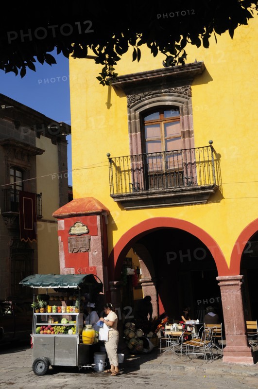 Mexico, Bajio, San Miguel de Allende, El Jardin Part view of yellow painted facade of colonial mansion with French window and balcony with fruit juice vendor in street below. Photo : Nick Bonetti