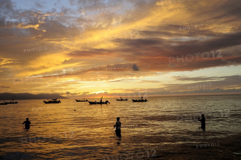 Mexico, Jalisco, Puerto Vallarta, Fishermen standing in sea with fishing boats at sunset. Photo : Nick Bonetti