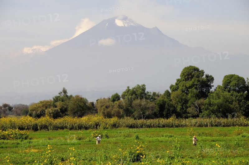 Mexico, Puebla, Popocatepetl, View towards volcanic cone of Popocatepetl with figures working in the fields in the foreground. Photo : Nick Bonetti