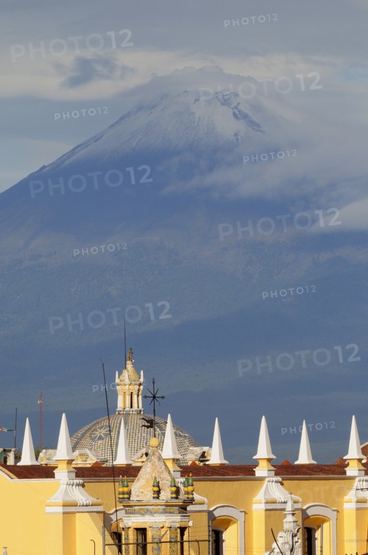 Mexico, Puebla, View of volcanic peak of Popocatepetl wreathed in cloud with Puebla rooftops in foreground. Photo : Nick Bonetti