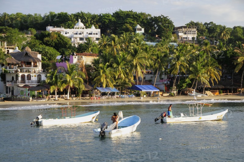Mexico, Oaxaca, Puerto Escondido, Fishing boats in bay at Playa Marinero lined with cafes bars and other buildings amongst palm trees. Photo : Nick Bonetti