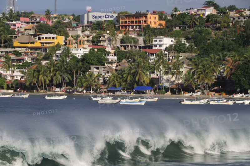 Mexico, Oaxaca, Puerto Escondido, Playa Principal Breaking waves and boats overlooked by buildings amongst palm trees.. Photo : Nick Bonetti