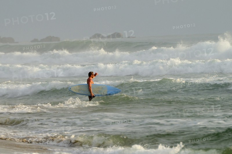 Mexico, Oaxaca, Puerto Escondido, Surfer walking through surf carrying board. Photo : Nick Bonetti