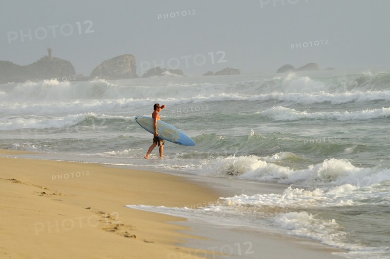 Mexico, Oaxaca, Puerto Escondido, Surfer walking into surf carrying board. Photo : Nick Bonetti