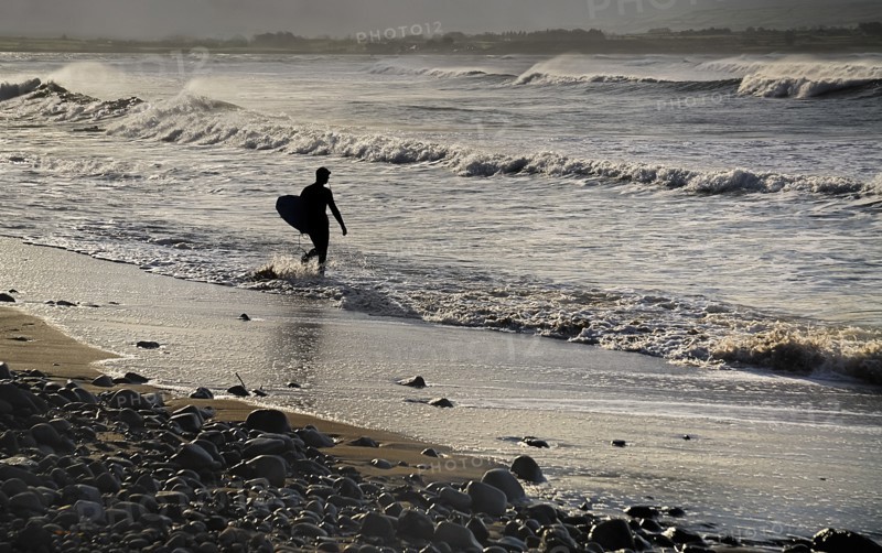 Ireland, County Sligo, Strandhill, Silhouette of surfer with surfboard heading into the sea. Photo : Hugh Rooney