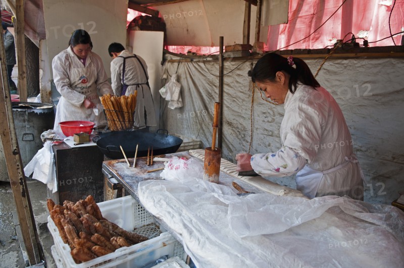 China, Jiangsu, Nanjing, Road-side bakery shop baker cutting strips of dough that will be twisted and deep-fried in a wok to ptoduce Yu Tiao a popular breakfast bread usually eaten with warm soyamilk or porridge or Xi Fan Bundles of Yu Tiao in baskets ready for sale. 
Photo Trevor Page / Eye Ubiquitous