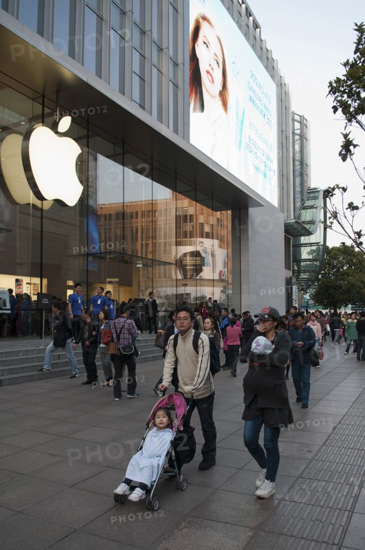China, Shanghai, Modern young Chinese family with daughter in stroller and infant in sling stroll past the Apple store on Nanjing Lu Store staff and Security on steps at entrance evening light. 
Photo Trevor Page / Eye Ubiquitous
