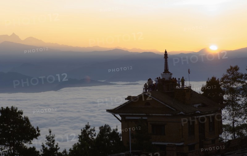 Nepal, Nagarkot, Sunrise view across clouded valley towards Himalayan mountains with Buddhist Stupa on top of building. 
Photo Nic I Anson / Eye Ubiquitous