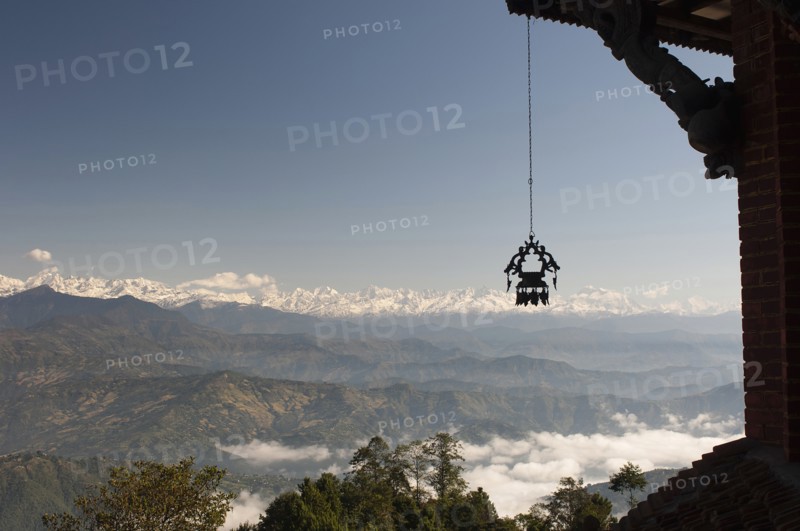 Nepal, Nagarkot, View across clouded valley towards Himalayan mountains wind chime hanging from traditionally carved corner of building in foreground. . 
Photo Nic I Anson / Eye Ubiquitous