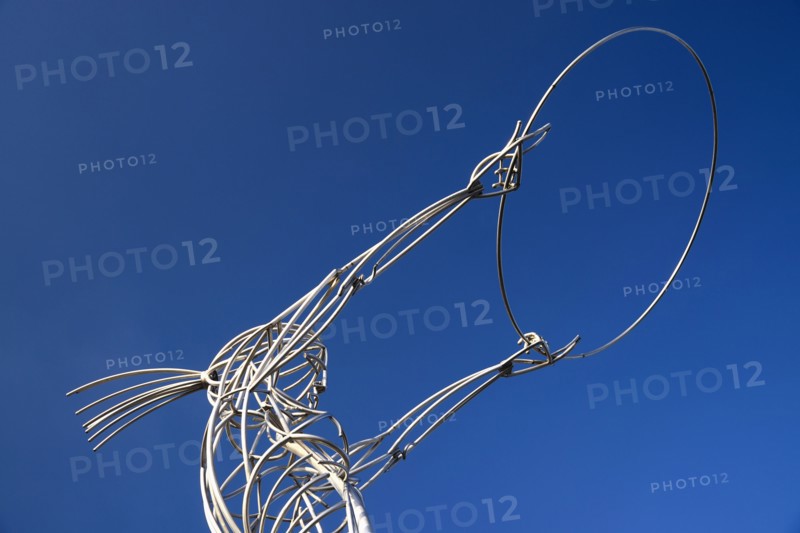 Ireland, North, Belfast, Ring of Thanksgiving sculpture  angular low viewpoint of modern metal sculpture depicting female figure holding up hoop against cloudless blue sky.