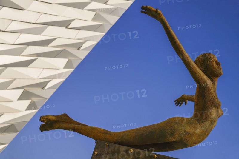 Ireland, North, Belfast, Titanic Quarter  Titanic Belfast Visitor Experience  Titanica sculpture by Rowan Gillespie with a section of the building and blue sky in the background.