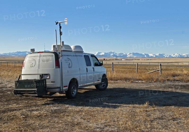 Canada, Alberta, Blood Reserve, Fracking for oil and gas on the Blood Tribe Indian Reserve at the edge of the Bakken Play. Oil company environmental air quality monitoring van with drilling site and snow-covered Rocky Mountains in the background. 
Photo Trevor Page