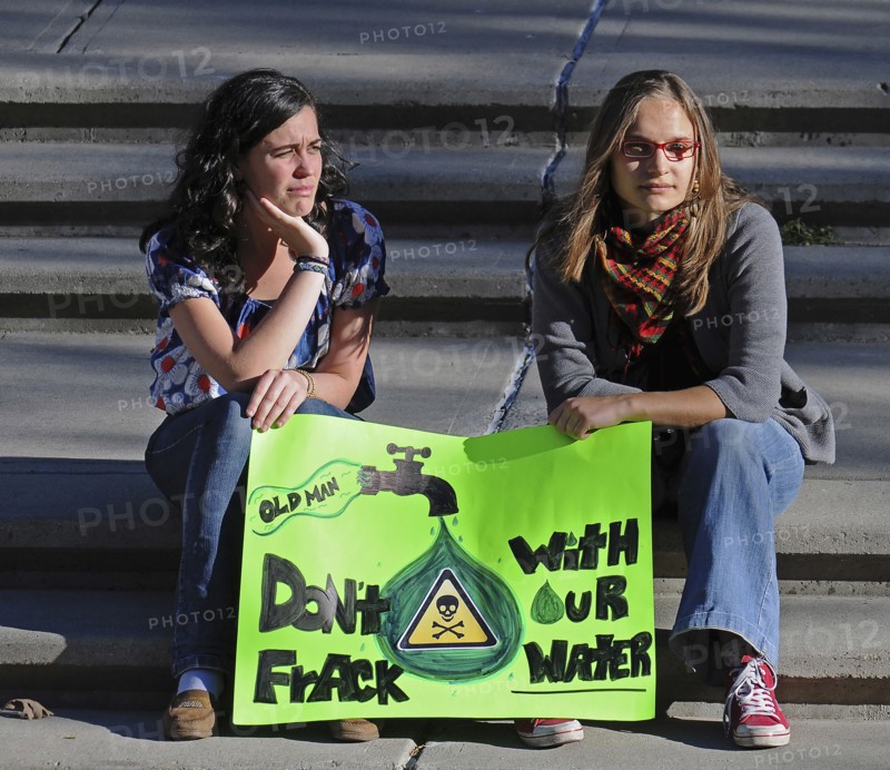 Canada, Alberta, Lethbridge, Two local women atsitting on stone steps at an anti-fracking demonstration holding a green protest sign. Oldman River  which runs through Lethbridge  is the source of the citys water supply.