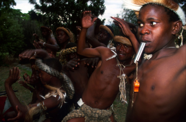 Zulu boy blowing on a whistle, dancers in the background