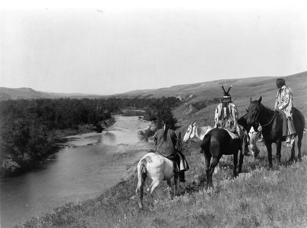 Three Piegan Indians and four horses on hill above river