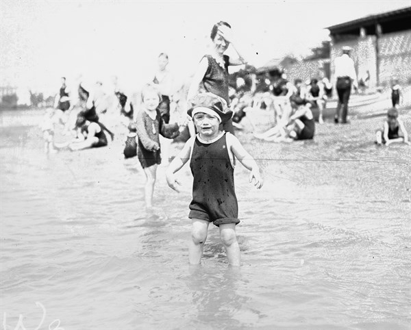 Young child at the edge of a beach crying as his family look on