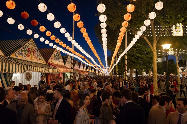 Spaniards celebrating in traditional clothes in front of lit marquees
