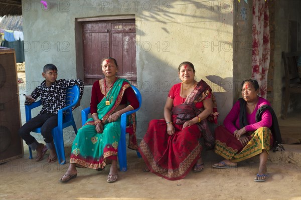 Nepalese women from the Tharu ethnic group sitting in front of a house during a wedding